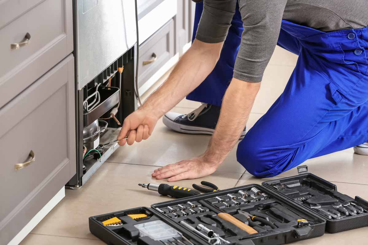 A refrigerator technician on his knees, working on a refrigerator