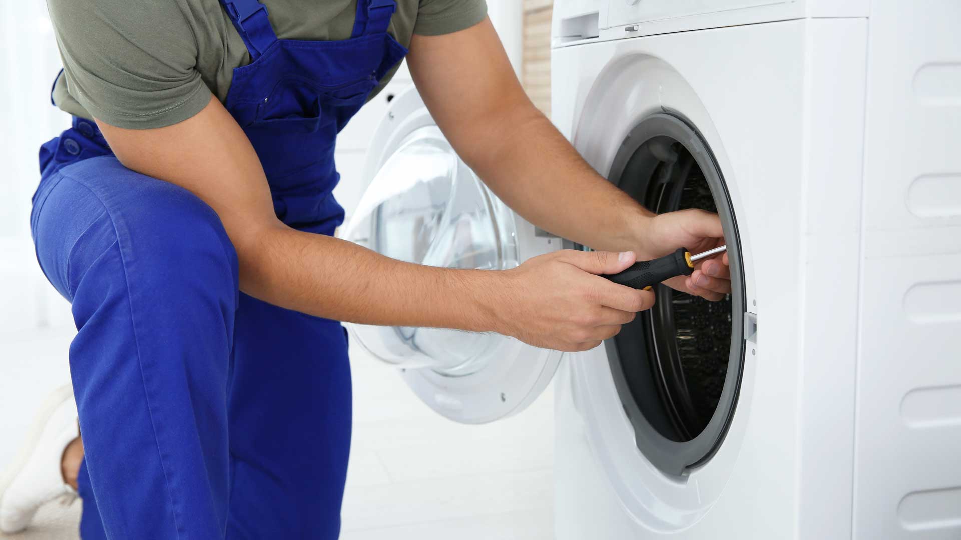 A technician in blue overalls repairing a washing machine